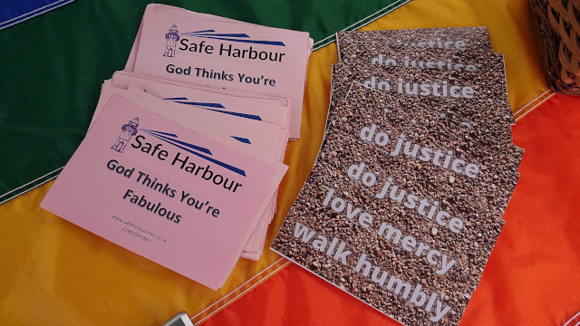 Safe Habour cards on a rainbow tablecloth. One side has the Safe Harbour logo and contact details, and the text 'God Thinks You're Faboulous'. The other side has the text 'do justice, love mercy, walk humbly'.